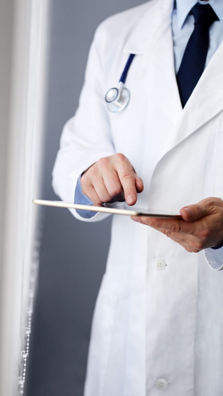 Male doctor working on a digital tablet near a window Male doctor working on a digital tablet near a window